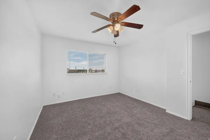 Neutral wall paint, ceiling fan with integrated lighting, window with blinds, and grey carpeting
