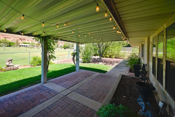 Covered patio featuring string lighting, brick paver flooring, and direct access to a grassy yard