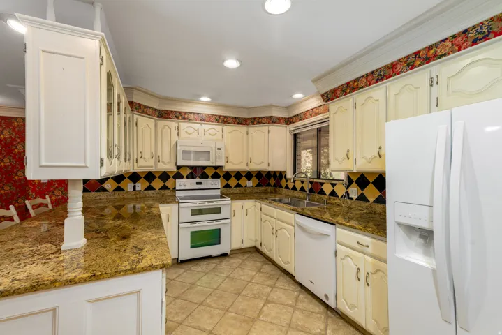 Expansive kitchen with granite countertops, built-in double oven, tile flooring, and integrated white appliances