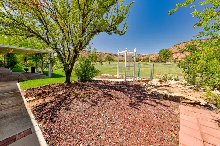 Expansive outdoor space featuring a covered patio, mature trees, and a red rock landscape with a decorative arbor and fencing