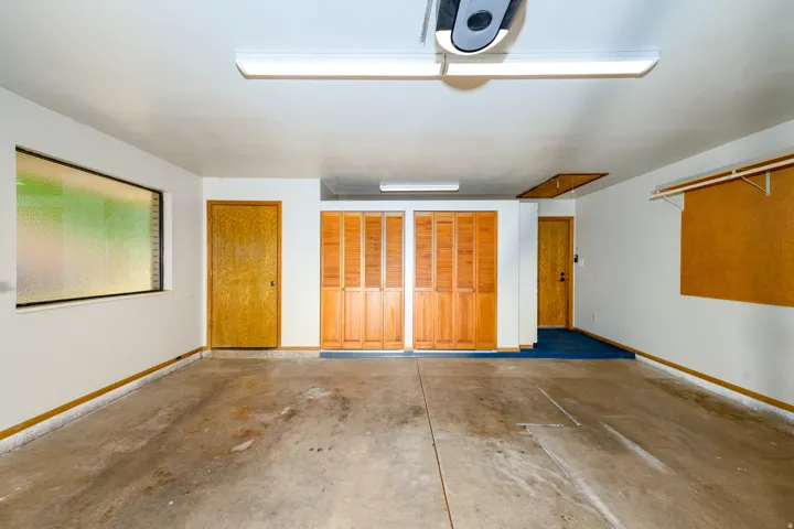 Attached garage with concrete flooring, two wood panel doors, two bi-fold wood doors, and a translucent window