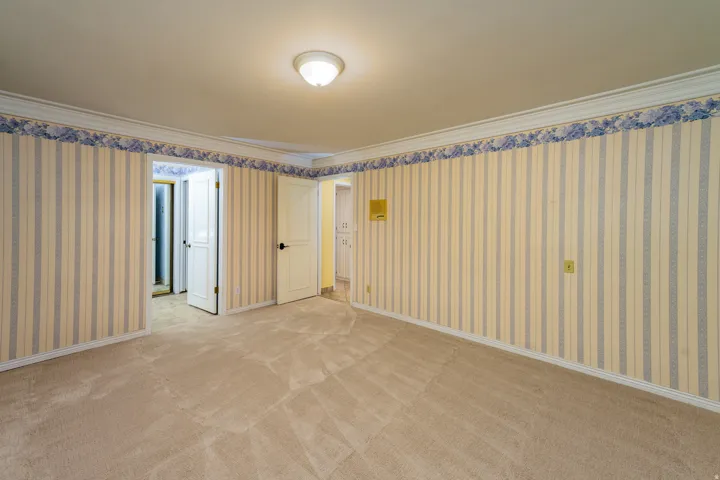 Recessed ceiling light fixture, crown molding, striped wallpaper, and carpet flooring