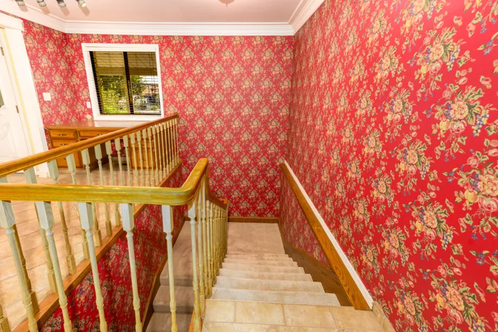 Staircase featuring wood railings and balusters, carpeted treads, and floral-patterned wallpaper