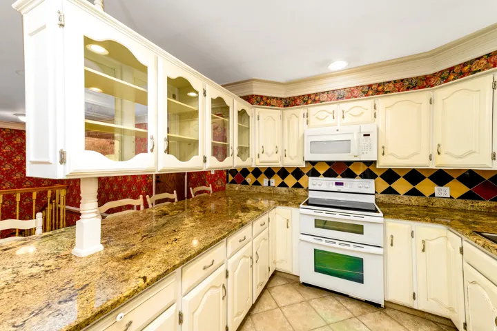 Cream-colored cabinetry with decorative molding, glass-front display cabinets, granite-finish countertops, built-in microwave, and tile flooring