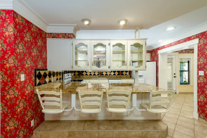 Kitchen featuring a breakfast bar with seating, white cabinetry with glass inserts, and a tiled backsplash