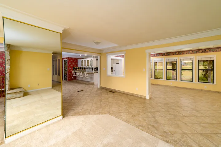 Expansive room featuring a mirrored wall, crown molding, and a combination of carpet and tiled flooring