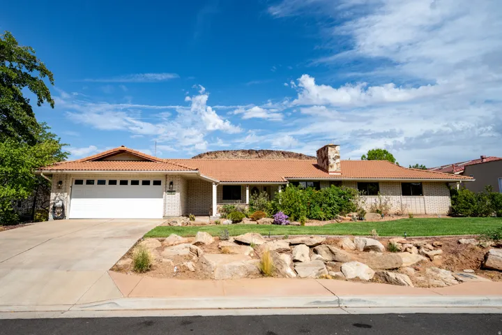 Front exterior featuring a terracotta tile roof, brick facade, attached garage, concrete driveway, and landscaped front yard with rock features
