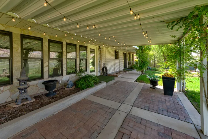 Covered patio with string lighting, brick paver flooring, stone accent wall, multiple windows, and exterior entry door