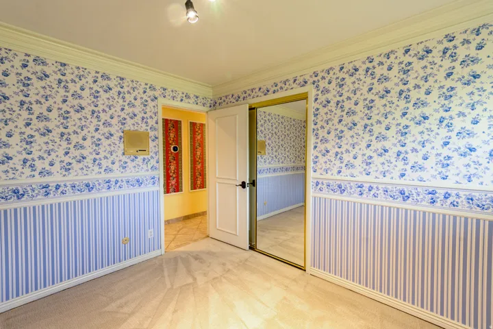 Carpeted room featuring crown molding, two-tone floral and striped wallpaper, a built-in closet with mirrored sliding doors, and a paneled interior door