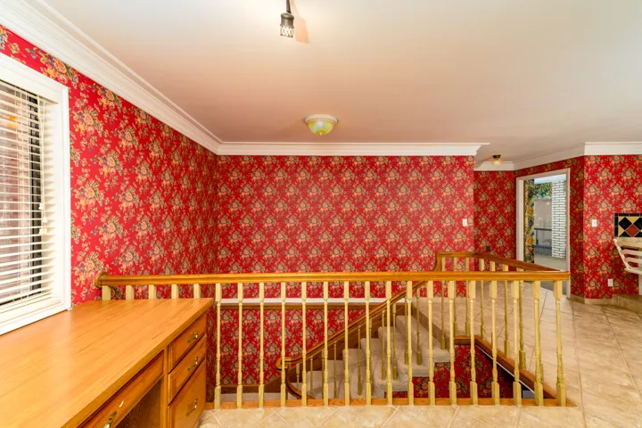 Staircase with wood railing, patterned wall covering, tile flooring, and a built-in desk with drawers