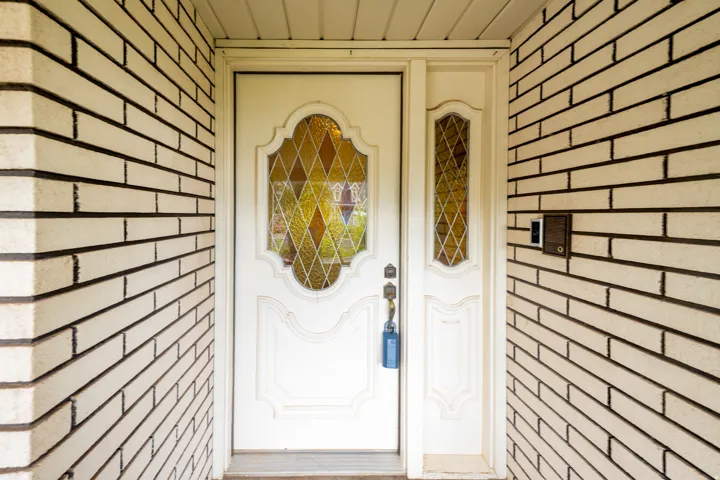 Entryway featuring a decorative front door with leaded glass panels, an adjacent sidelight, and light-toned brickwork