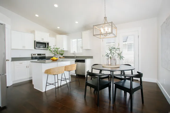Kitchen featuring white cabinetry, stainless steel appliances, dark wood-finish flooring, a kitchen island, and a dining area with a modern chandelier