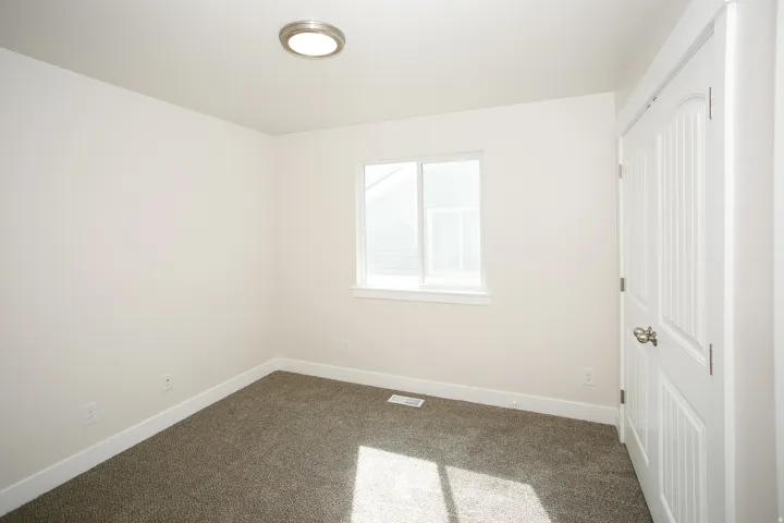 Neutral wall paint, textured carpet, window with white trim, flush mount ceiling light, and a paneled interior door