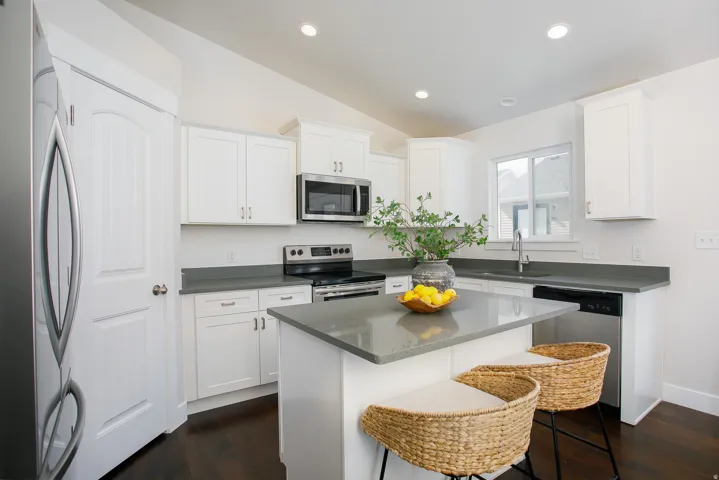 Kitchen featuring white cabinetry, stainless steel appliances, a center island with countertop seating, recessed lighting, and dark wood-finish flooring