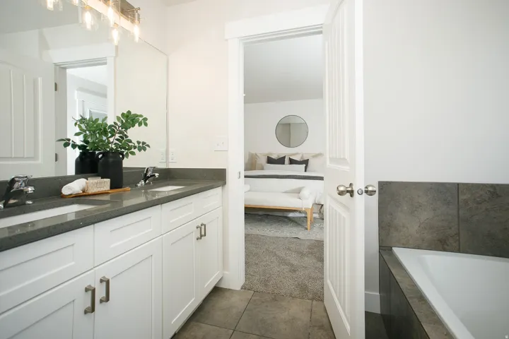 Bathroom featuring a dual vanity with undermount sinks, a large mirror, a built-in bathtub, and tile flooring