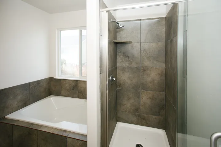 Built-in bathtub with tiled surround, separate shower with tile enclosure, shower pan, and glass door