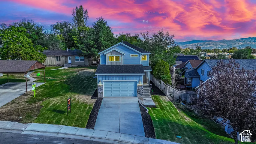 Two-story residence featuring a blue horizontal siding exterior, stone veneer accents, concrete driveway, attached two-car garage, and mountain backdrop