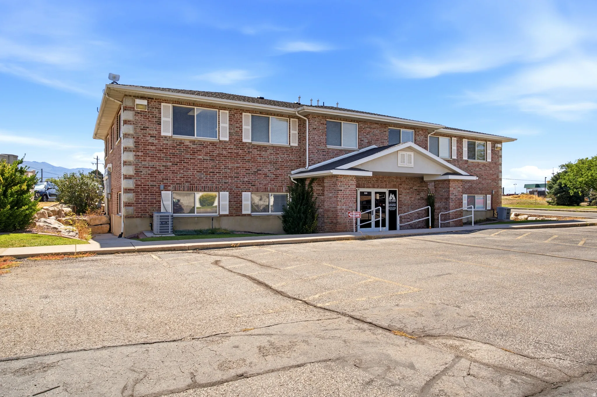 Brick facade with multiple windows, prominent entry with covered portico, dual-level structure, and an expansive paved parking area