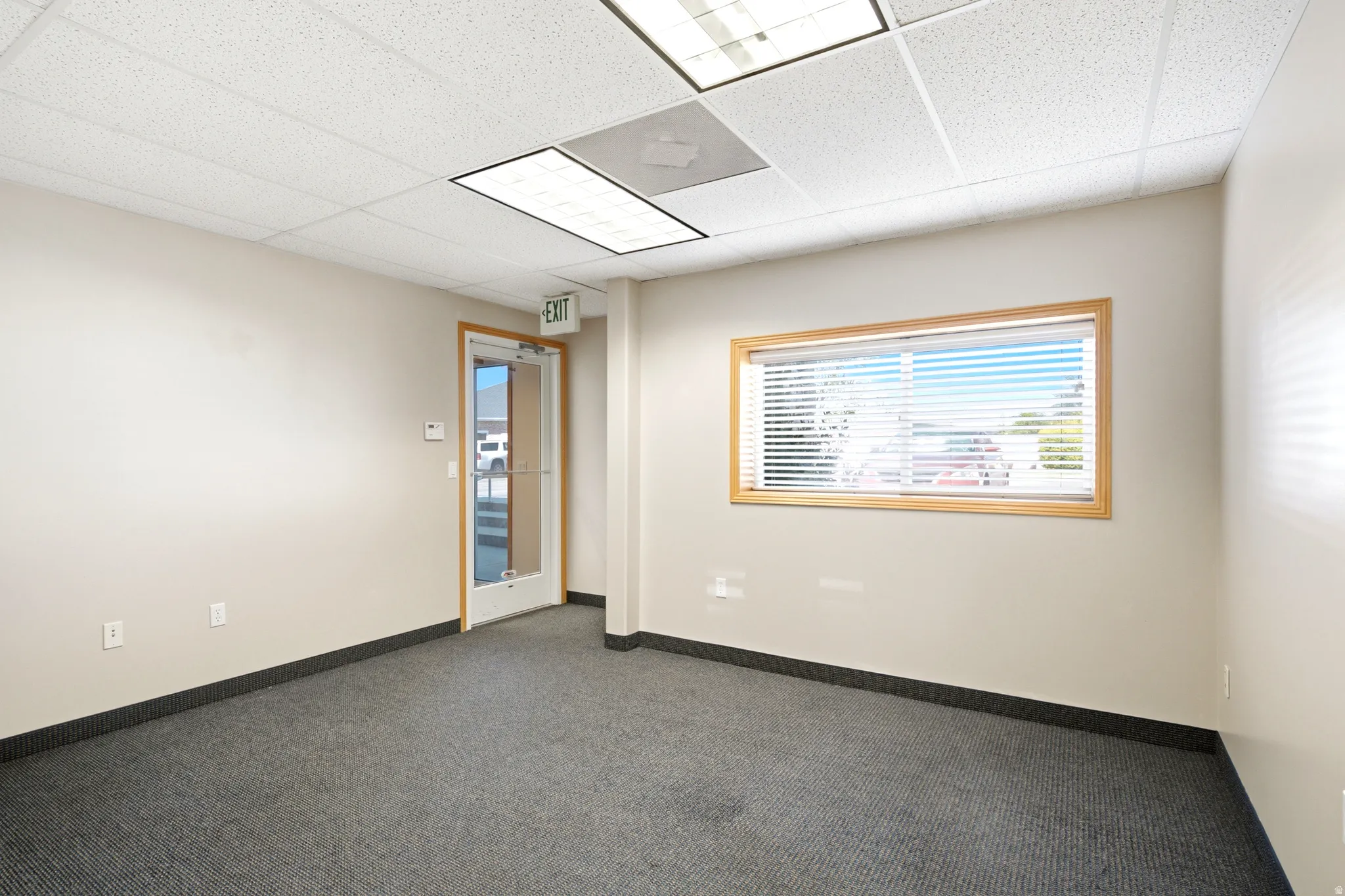 Commercial space featuring a drop ceiling, fluorescent lighting, neutral wall paint, and gray carpet