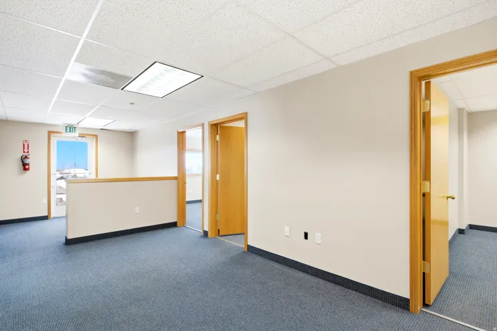 Blue carpet flooring, wood-finish doors, drop ceiling with recessed lighting, half-wall partition with wood-finish railing, and a window with exterior visibility