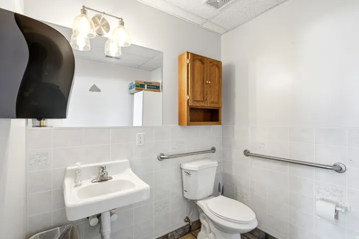 Wall-mounted sink with chrome faucet, light-toned wall tile, and built-in wood-finish cabinetry