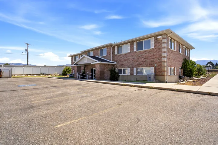 Brick exterior, multiple windows with white shutters, paved parking lot, concrete sidewalk, accessible ramp