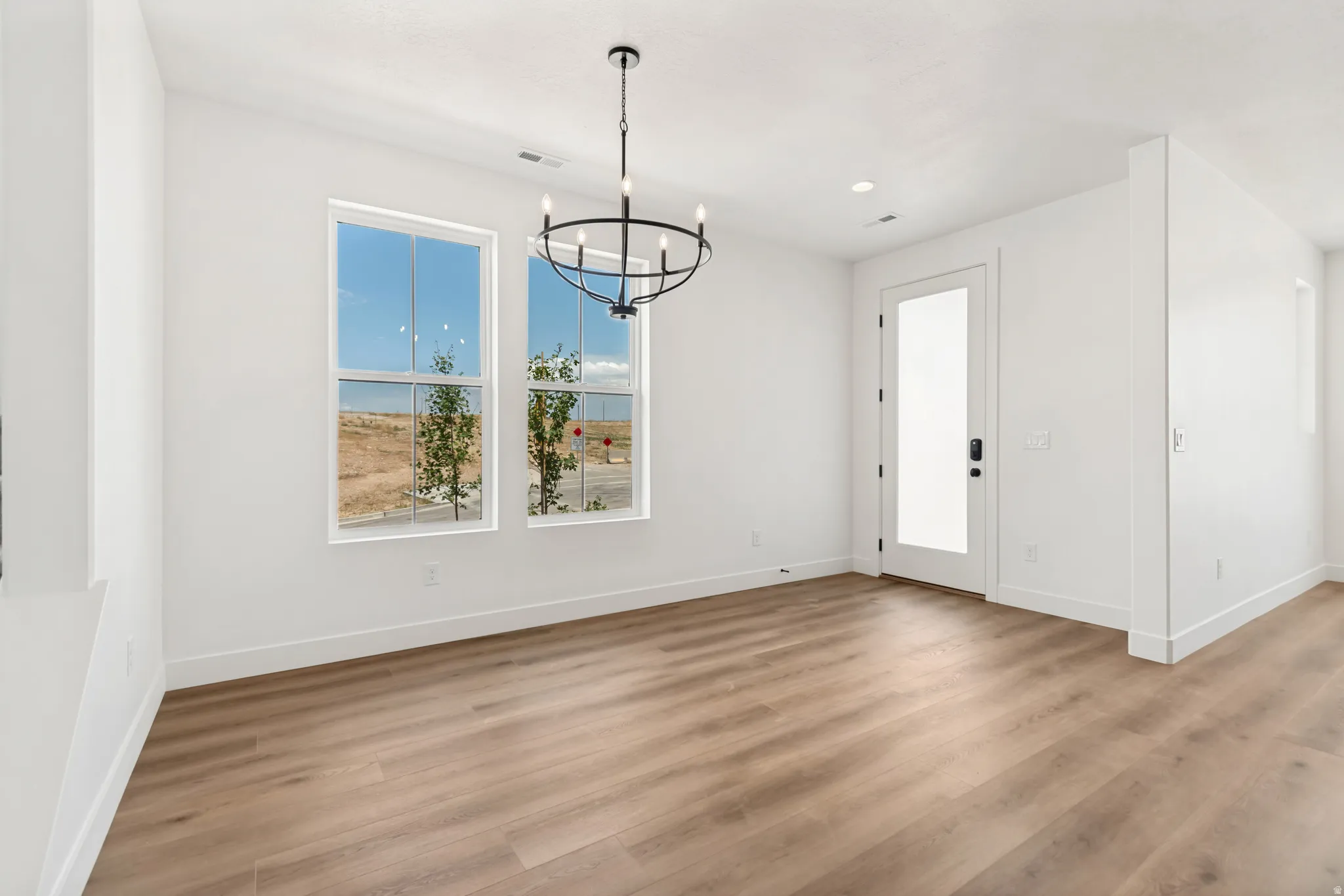 Wood-finish flooring, white walls, two double-hung windows, frosted glass panel door, and a black circular chandelier