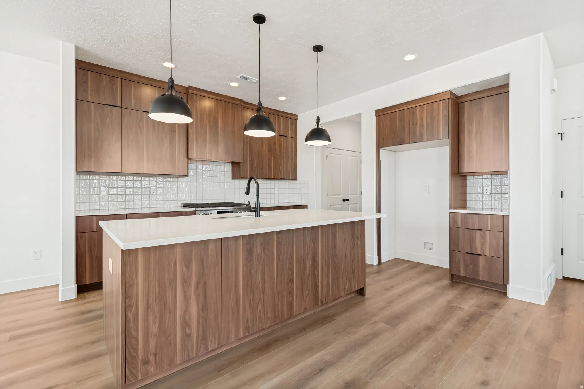 Kitchen featuring wood-finish cabinetry, a large center island with a light-toned countertop, a tile backsplash, and recessed lighting