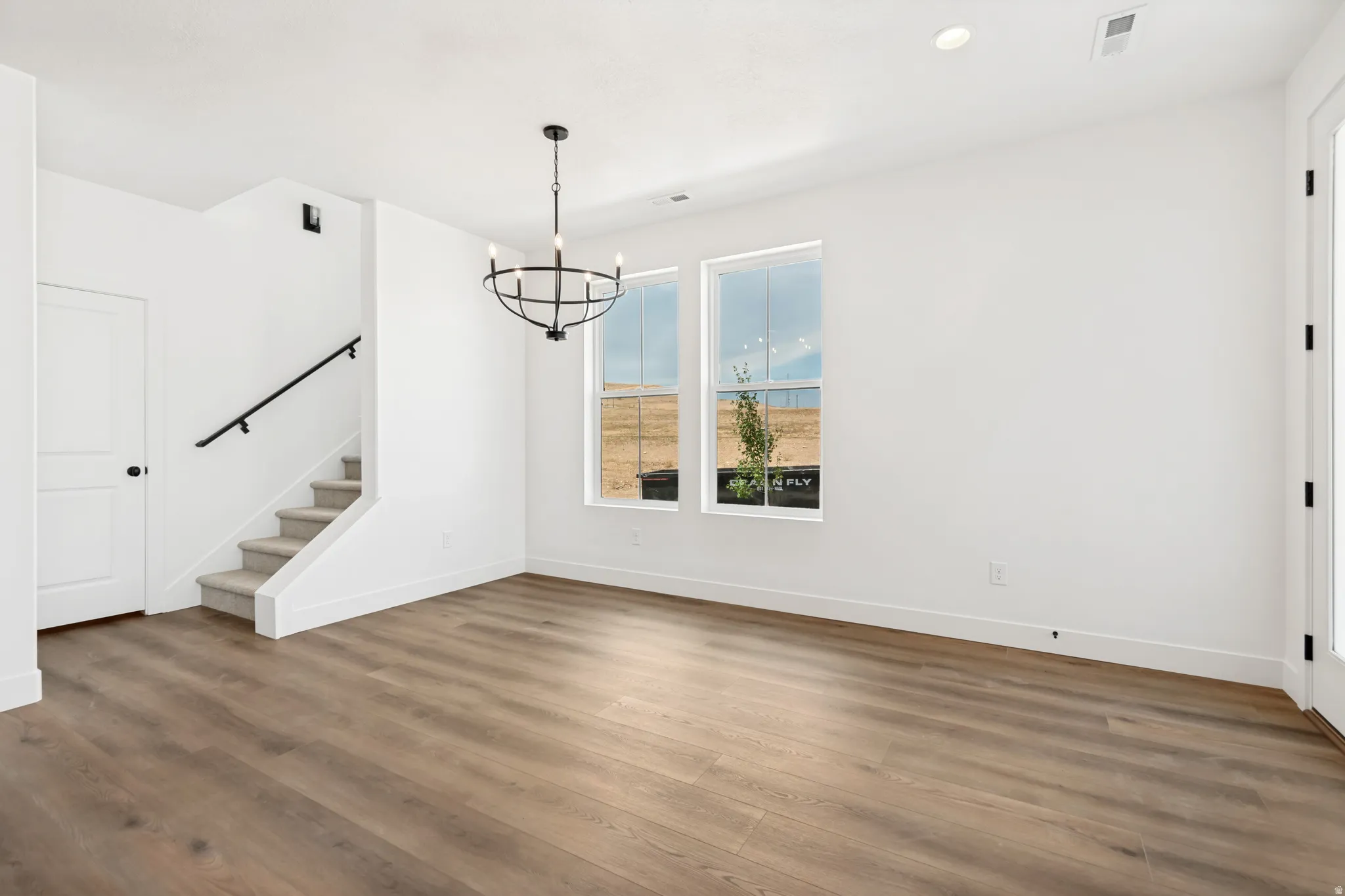 Wood-finish flooring, staircase with carpeted treads and black handrail, modern chandelier, recessed lighting, and white trim