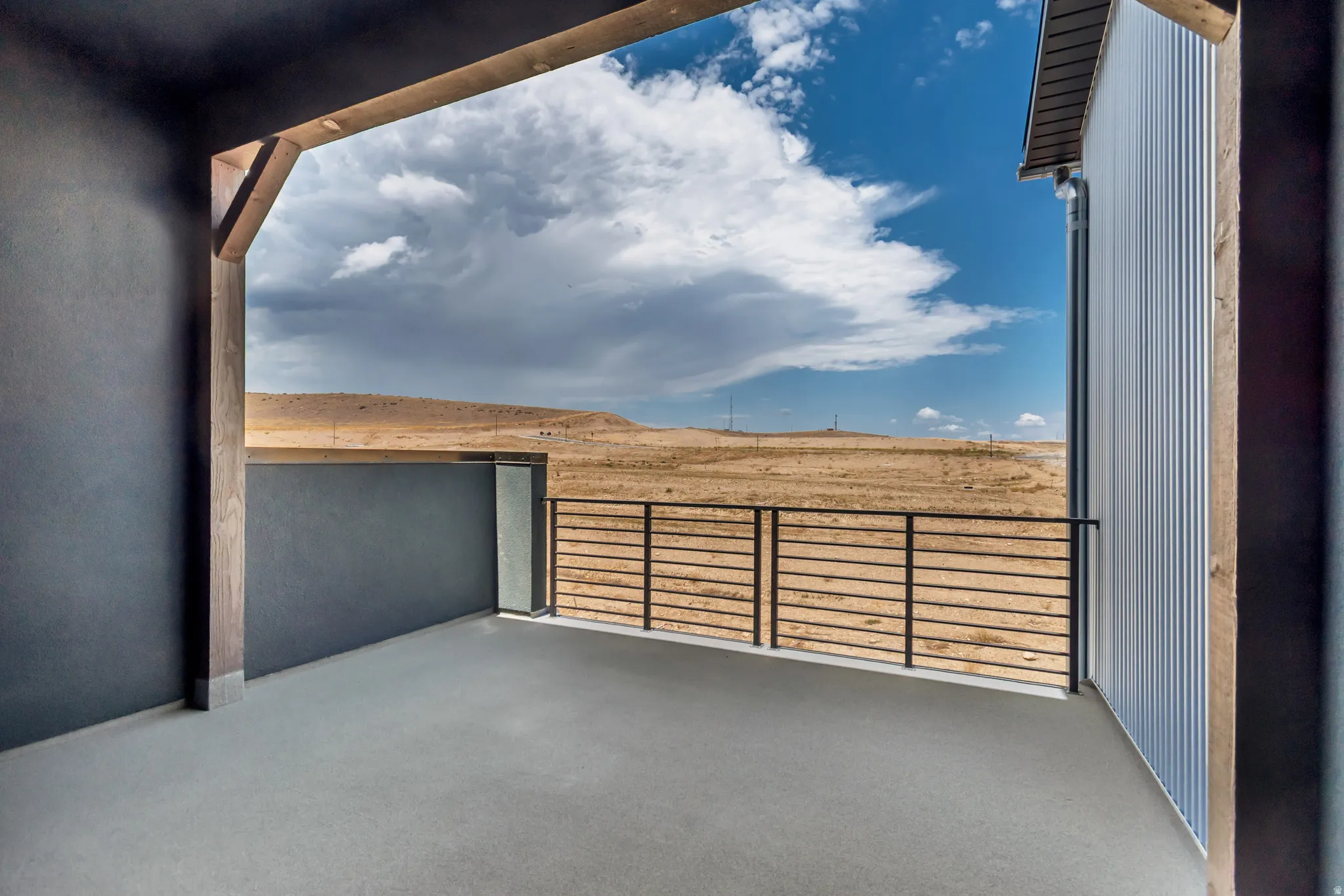 Outdoor balcony with concrete flooring, black metal railing, and a slatted wall detail