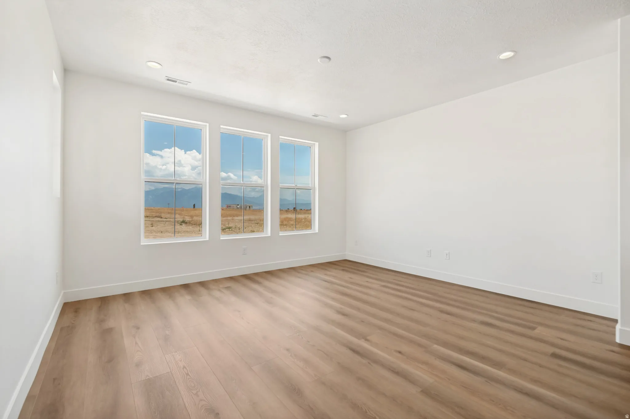 Neutral white walls, recessed ceiling lighting, three paneled windows, light wood-finish flooring