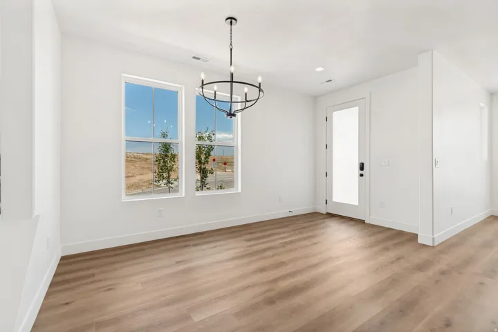 Wood-finish flooring, white walls, two double-hung windows, frosted glass panel door, and a black circular chandelier