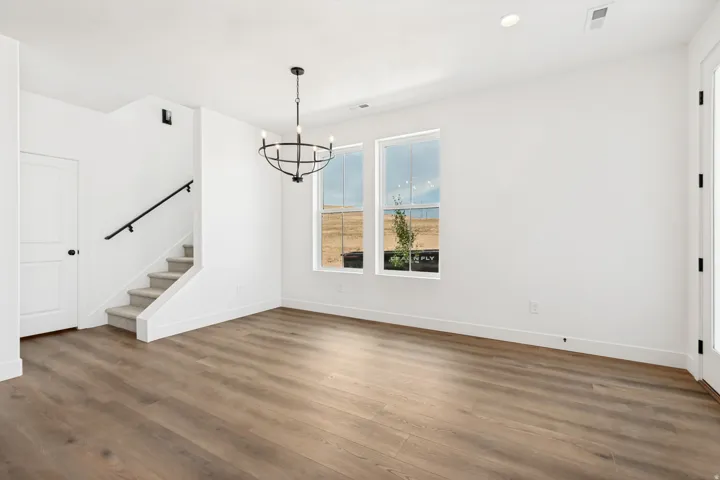 Wood-finish flooring, staircase with carpeted treads and black handrail, modern chandelier, recessed lighting, and white trim