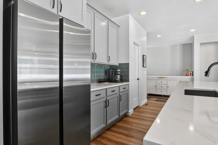 Stainless steel side-by-side refrigerator, two-tone cabinetry with matte black hardware, white stone-finish countertops, and wood-finish flooring