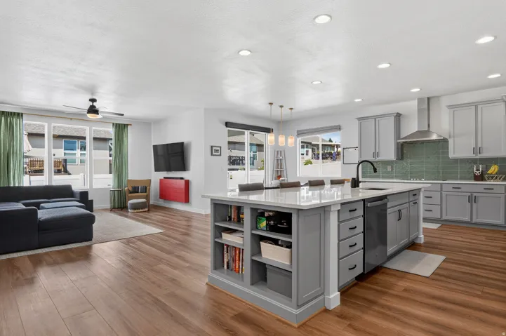 Open-concept floor plan featuring wood-finish flooring, a large kitchen island with built-in shelving, gray cabinetry, and recessed lighting