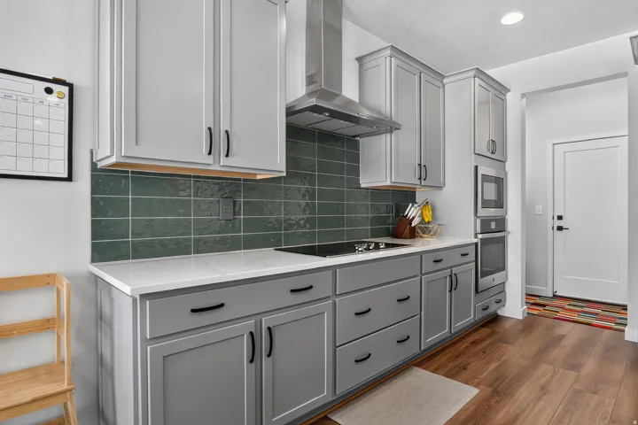 Kitchen featuring gray shaker-style cabinetry, white countertops, and a green subway tile backsplash