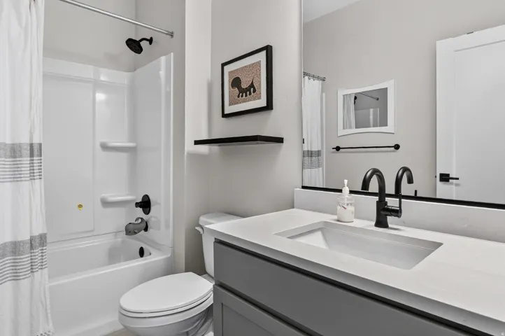 Bathroom featuring a white bathtub, integrated shower, built-in vanity with single basin, black matte fixtures, and a large wall-mounted mirror