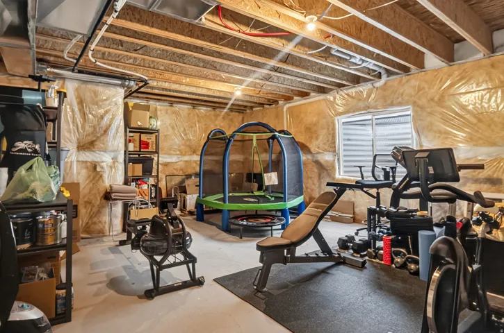 Unfinished basement space featuring exposed joists, visible insulation, and a window well