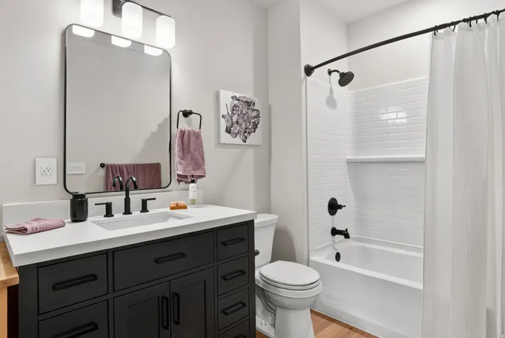 Contemporary vanity with an integrated sink and matte black fixtures, framed mirror, and a three-light vanity bar