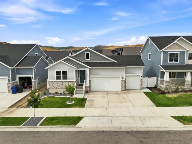 Contemporary exterior with light gray siding, stone veneer accents, an attached two-car garage, and a landscaped front yard