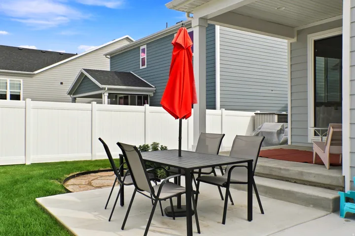 Concrete patio with a covered outdoor area, manicured lawn, and white privacy fencing