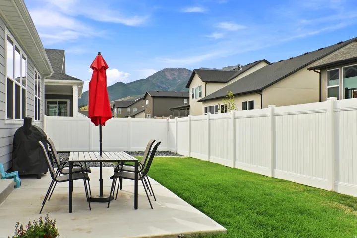 Concrete patio with a manicured lawn, white privacy fencing, and mountain scenery