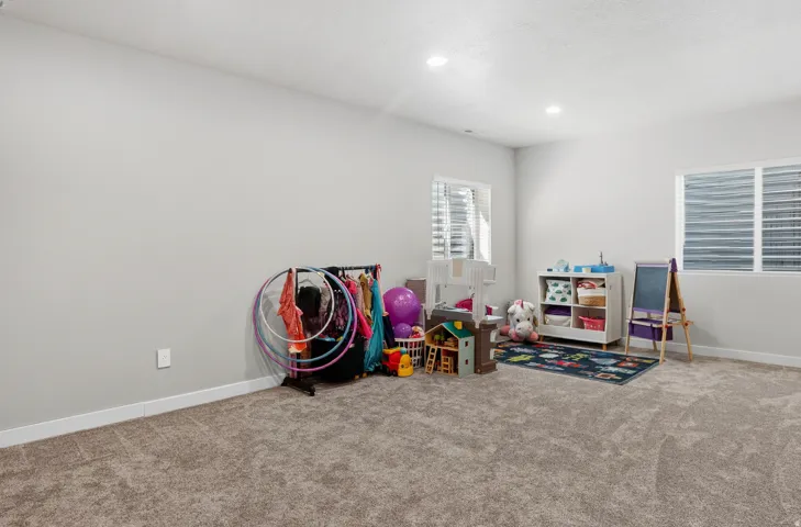 Carpeted room featuring light gray walls, two windows with horizontal blinds, and recessed lighting