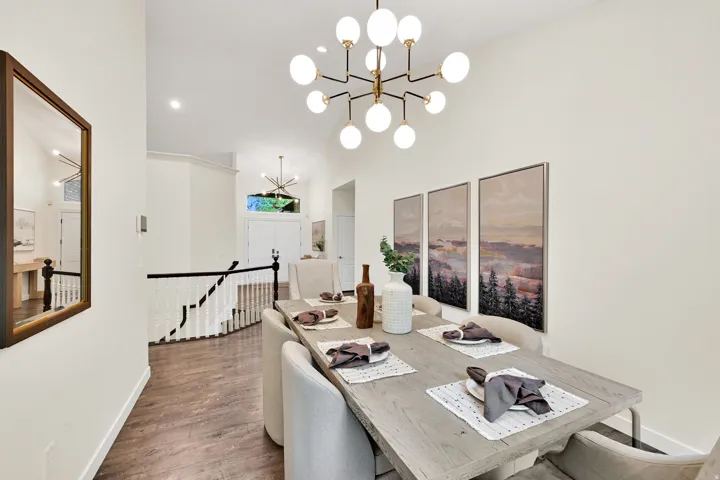Vaulted ceiling, wood-finish flooring, staircase with white spindles and dark wood banister, contemporary multi-bulb chandelier, and recessed lighting