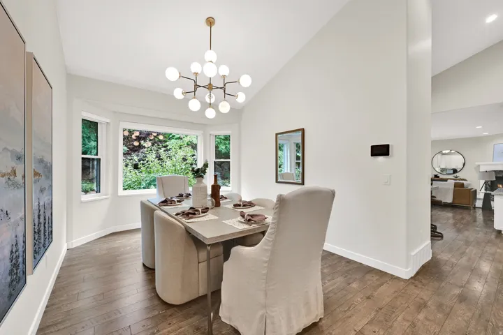 Dining area featuring a bay window, wood-finish flooring, vaulted ceiling, and a contemporary chandelier