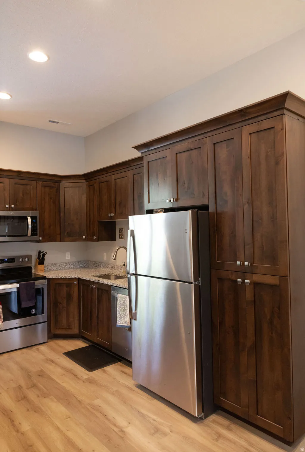 Kitchen featuring wood-finish flooring, dark wood cabinetry, granite-finish countertops, and stainless steel appliances