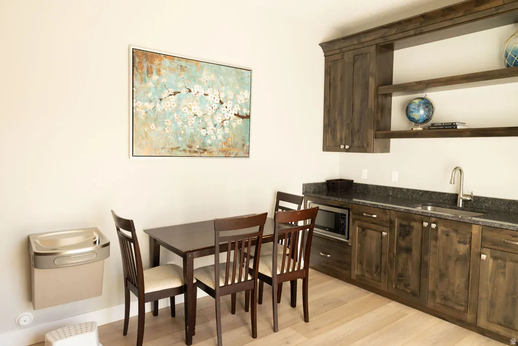 Built-in wet bar featuring dark wood-finish cabinetry, a stainless steel sink with a gooseneck faucet, and integrated microwave