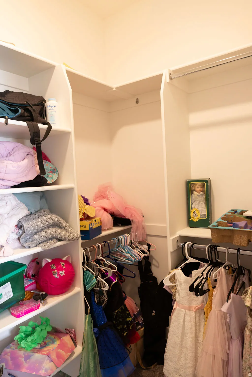 Walk-in closet featuring white built-in shelving, white walls, and multiple hanging rods