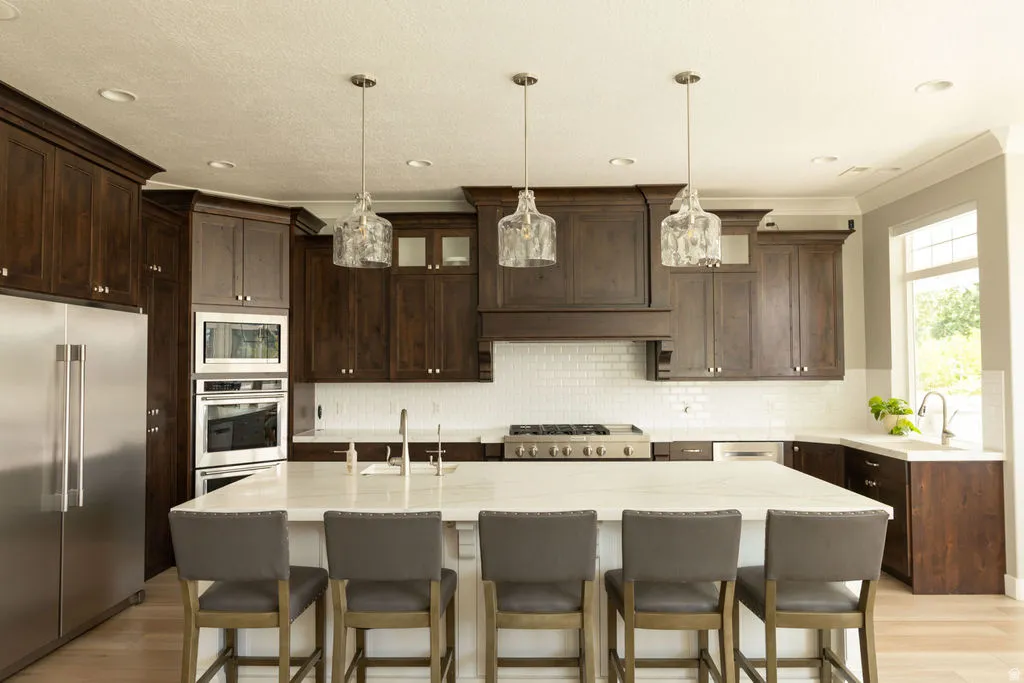 Spacious kitchen featuring dark wood cabinetry, stainless steel appliances, a white subway tile backsplash, and a large island with a light-colored countertop