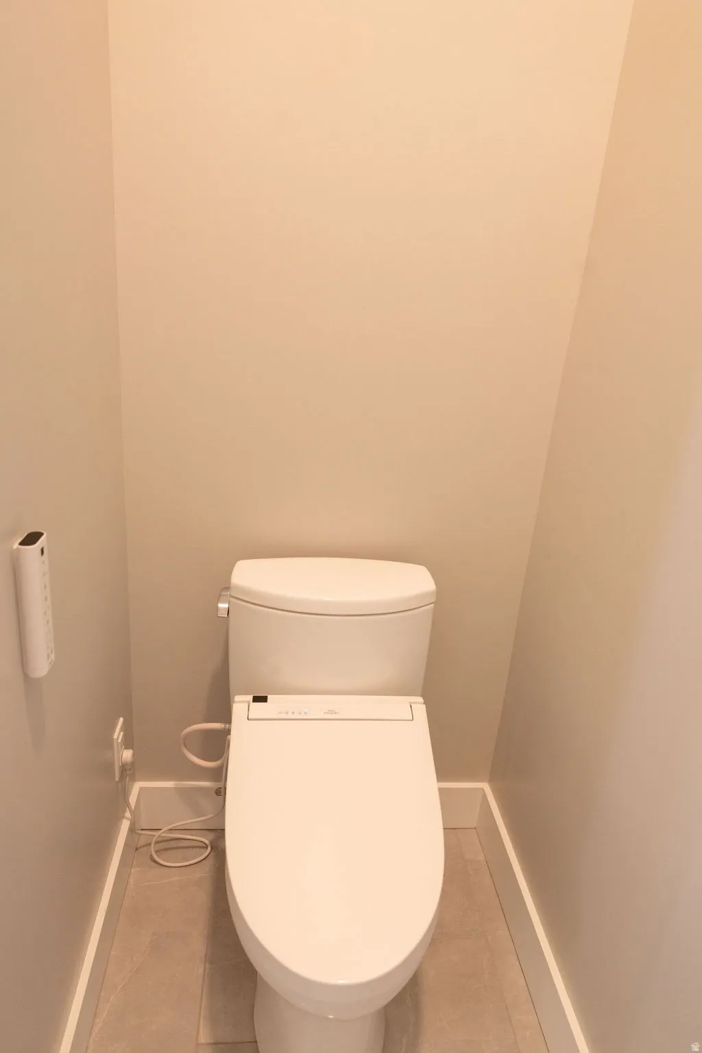 White toilet with bidet attachment and tile flooring